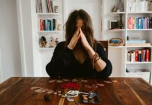 Emergency Love Spell for Broken Heart: Heal Fast and Attract New Love in 7 Days A woman in deep thought sits at a table with beads and a photo, conveying introspection. - emergency love spell for broken heart healing fast