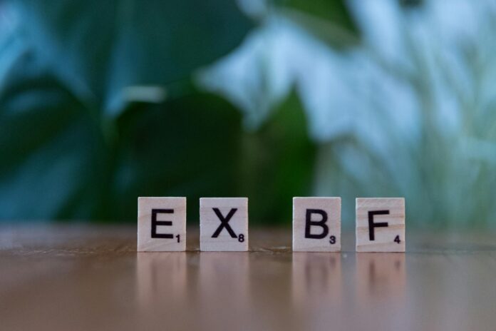 Close-up of Scrabble tiles spelling 'EXBF' on a wooden table with blurred background. - love spell to make my ex text me tonight