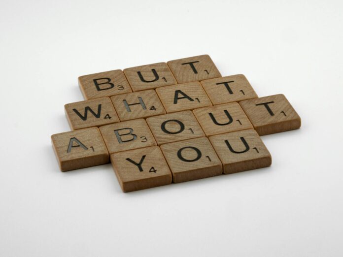 Close-up of wooden Scrabble tiles spelling 'But What About You' on a white surface. - make him think about me constantly spell