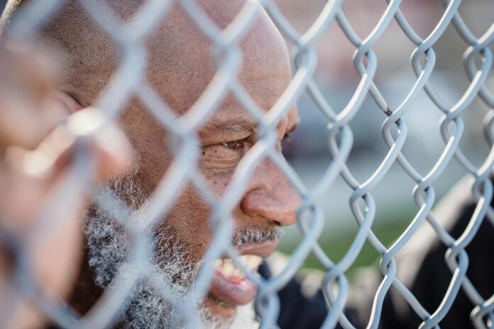 Close-up of mature man behind a metal fence, conveying deep thought and emotion. - obsession spells